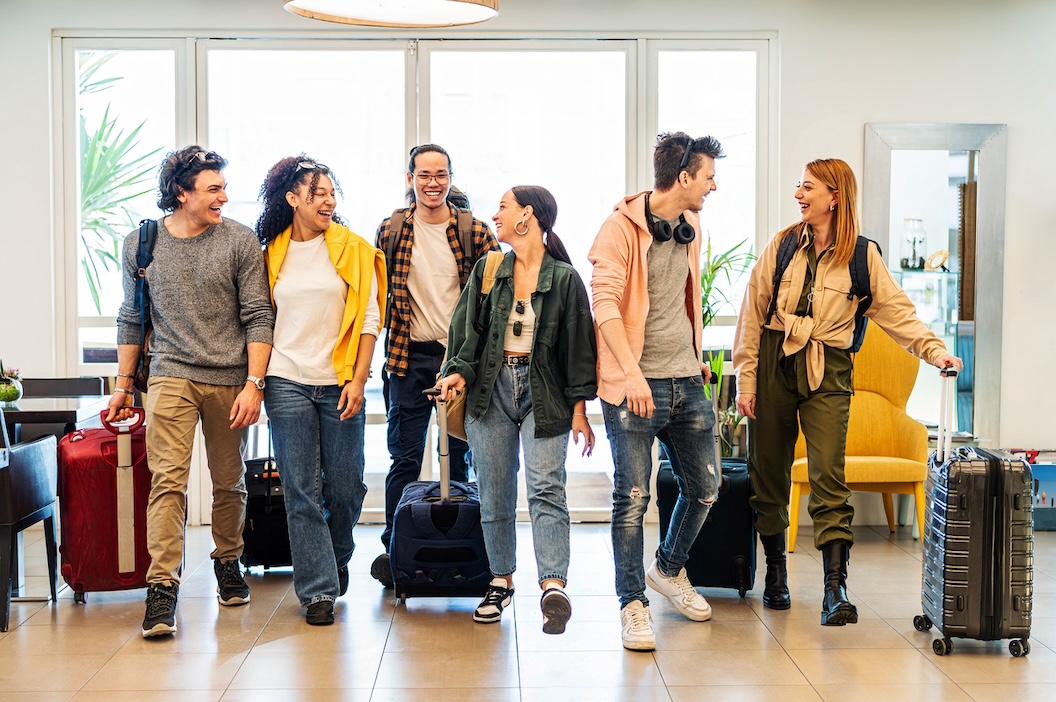 Group of young travelers smiling and arriving at a modern hotel lobby with suitcases, suggesting a group-friendly hotel stay experience.